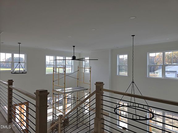 Interior view of a modern loft space with pendant lights, windows, and a railing. Scaffolding is visible.