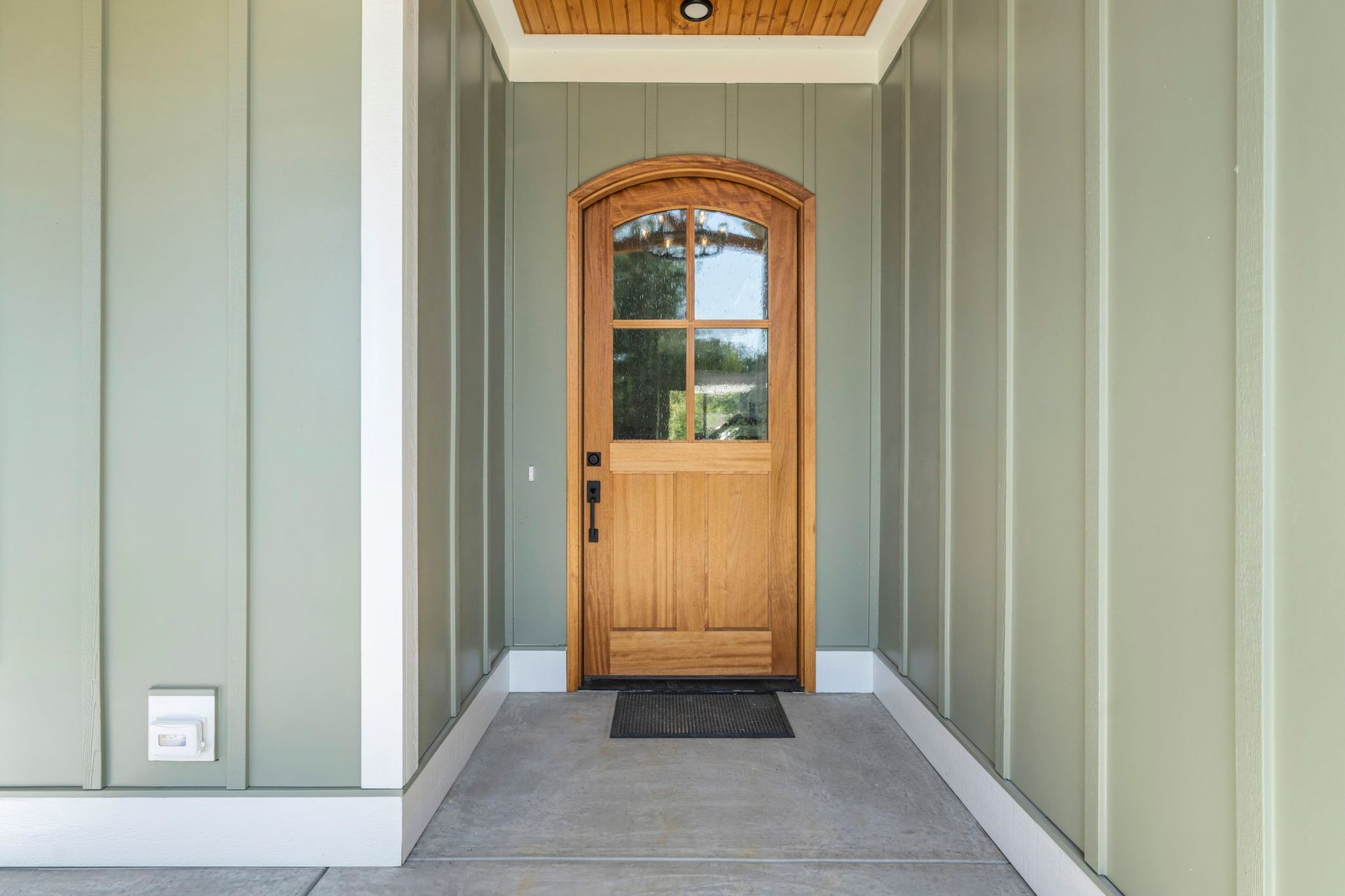 Wooden arched door with glass panels, centered in a sage green alcove.
