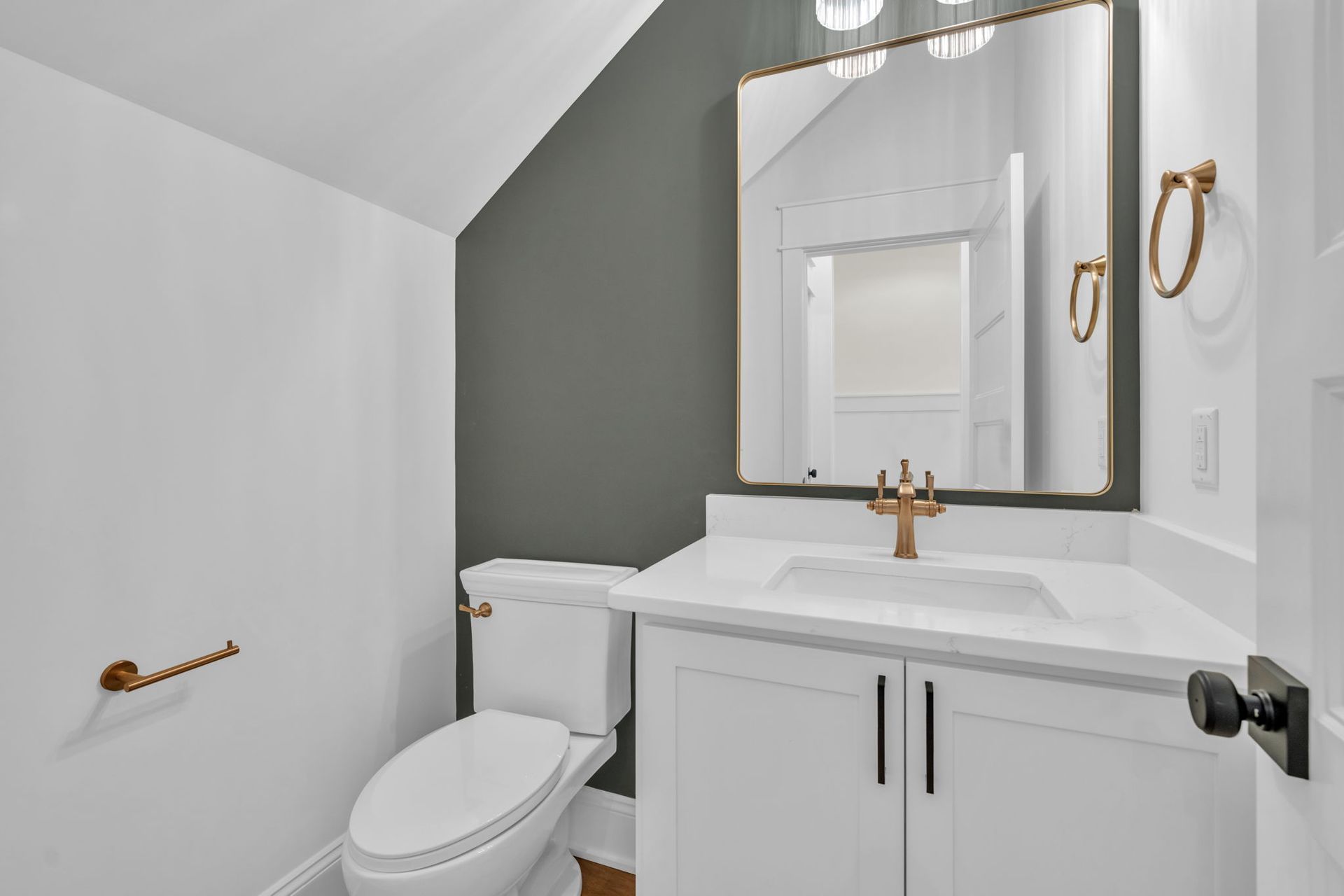 Powder room with white vanity, toilet, and walls. Gray accent wall, gold fixtures, and a mirror.