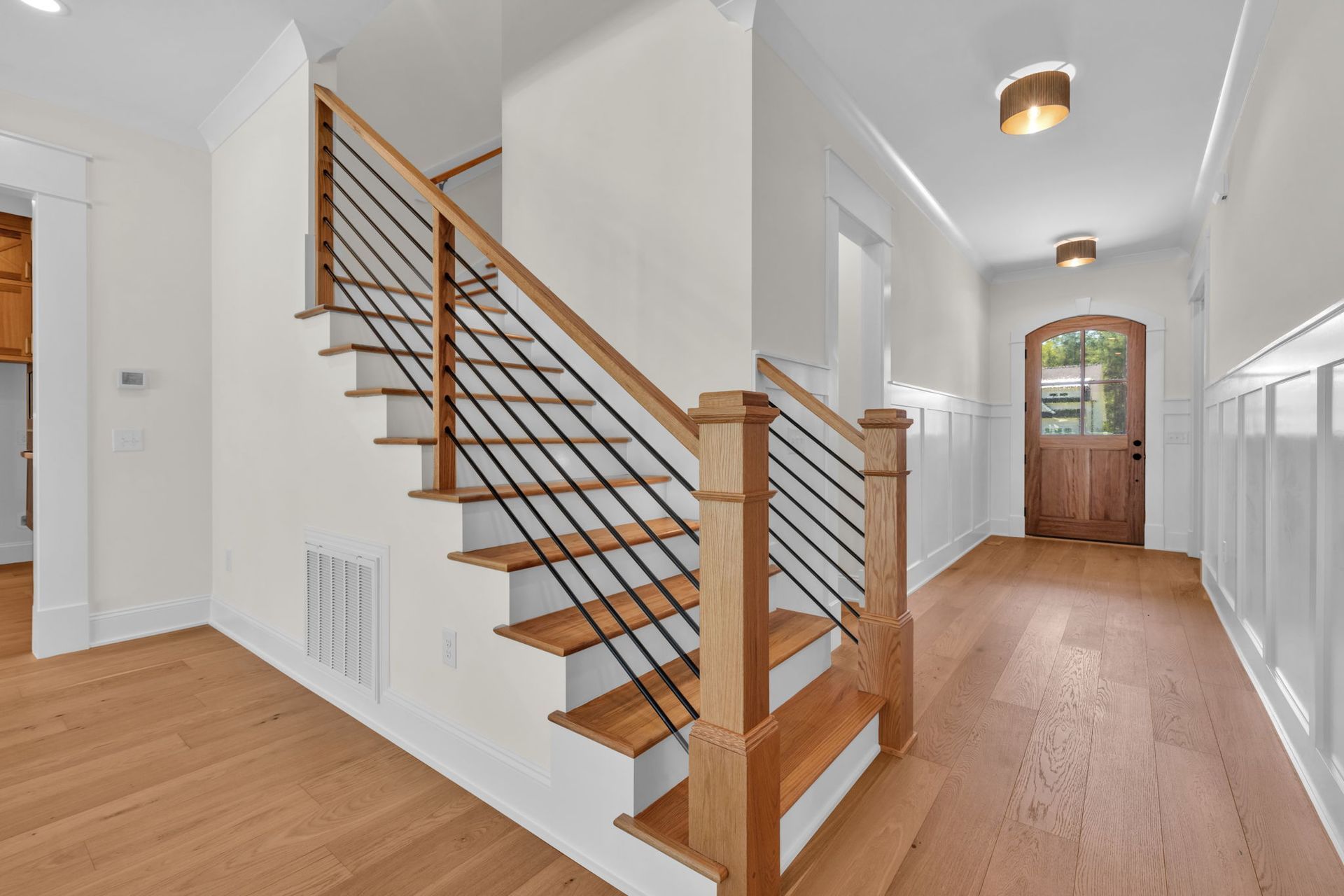 Wooden staircase with black railings in a bright entryway with light wood floors.