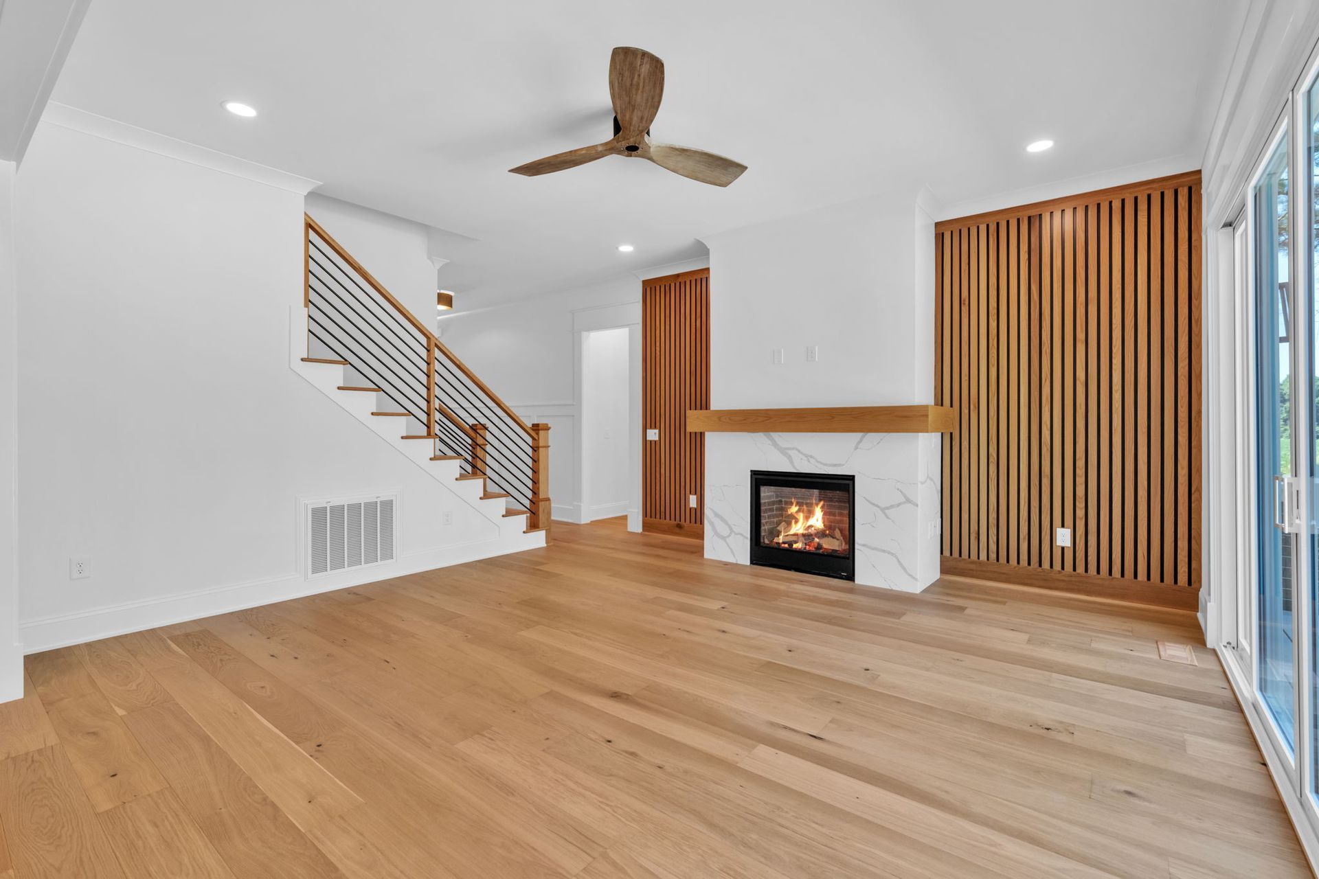 Spacious living room with hardwood floors, stairs with a modern railing, a fireplace, and a wooden accent wall.