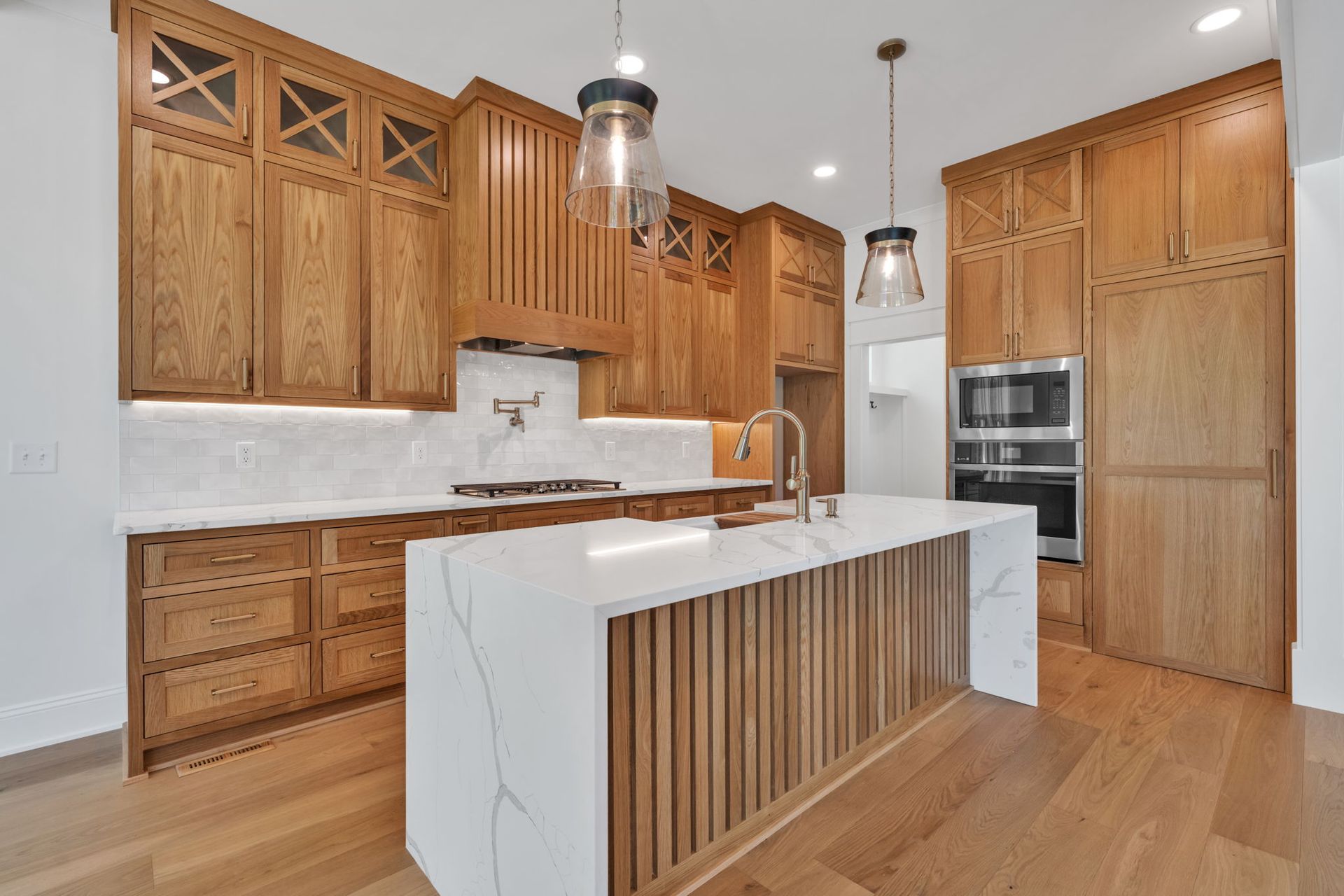 Wooden kitchen with white countertops, a central island, and two hanging lights.
