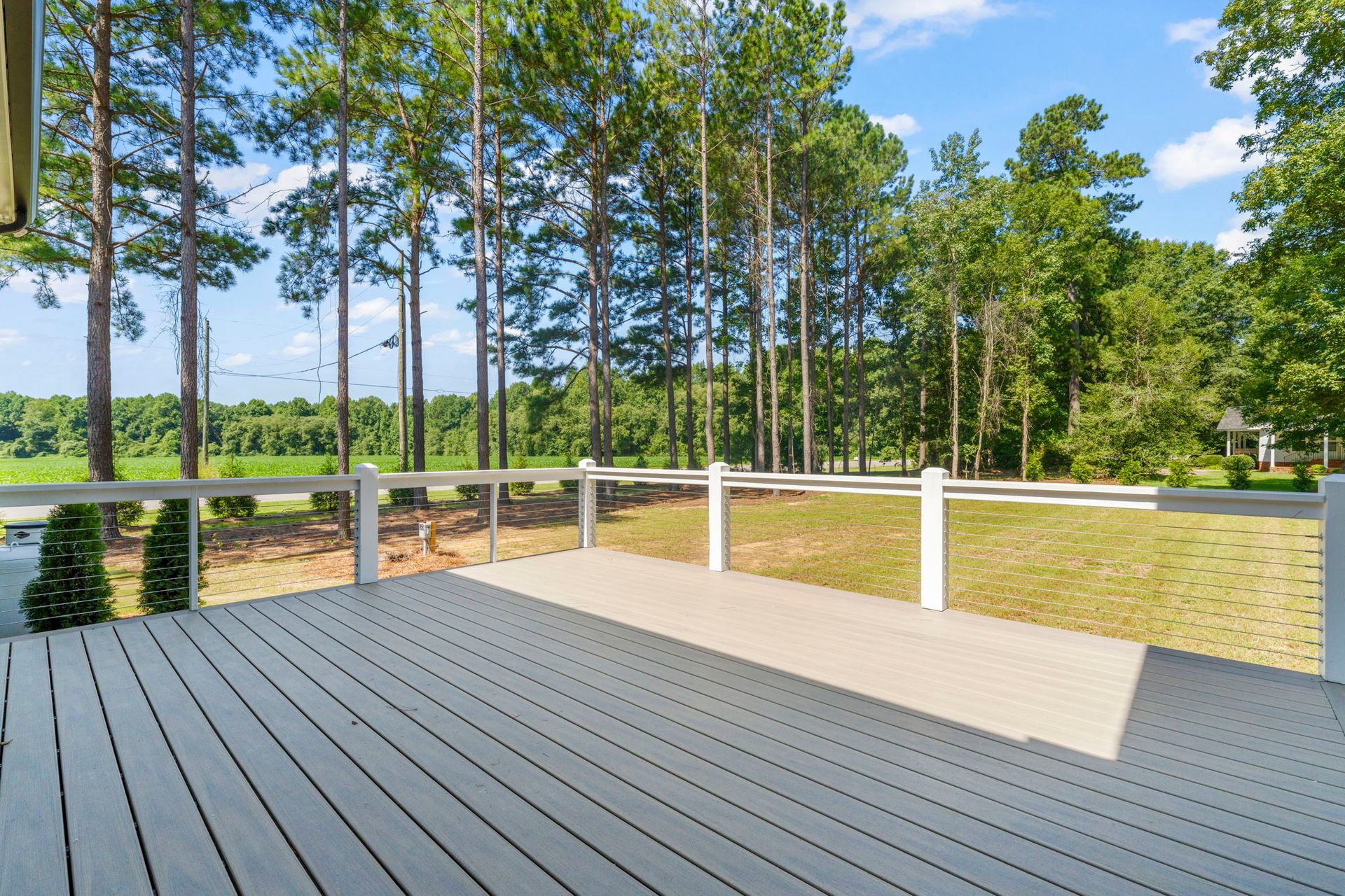 A gray wooden deck with white railings overlooks a grassy yard and tall trees.