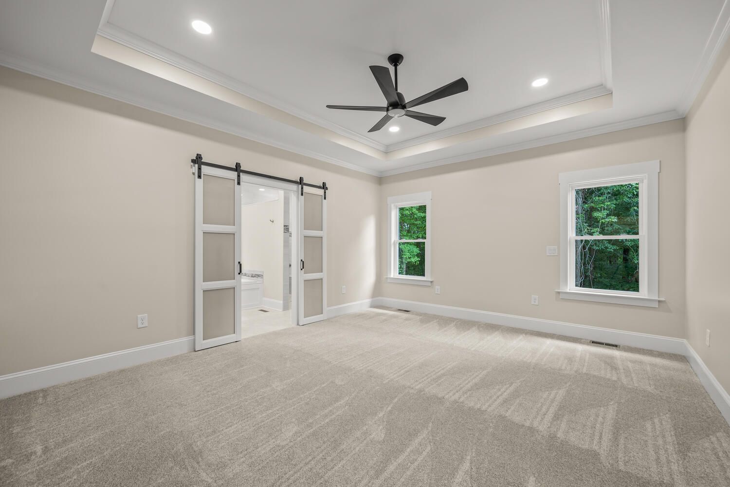 An empty bedroom with a ceiling fan and sliding barn doors.