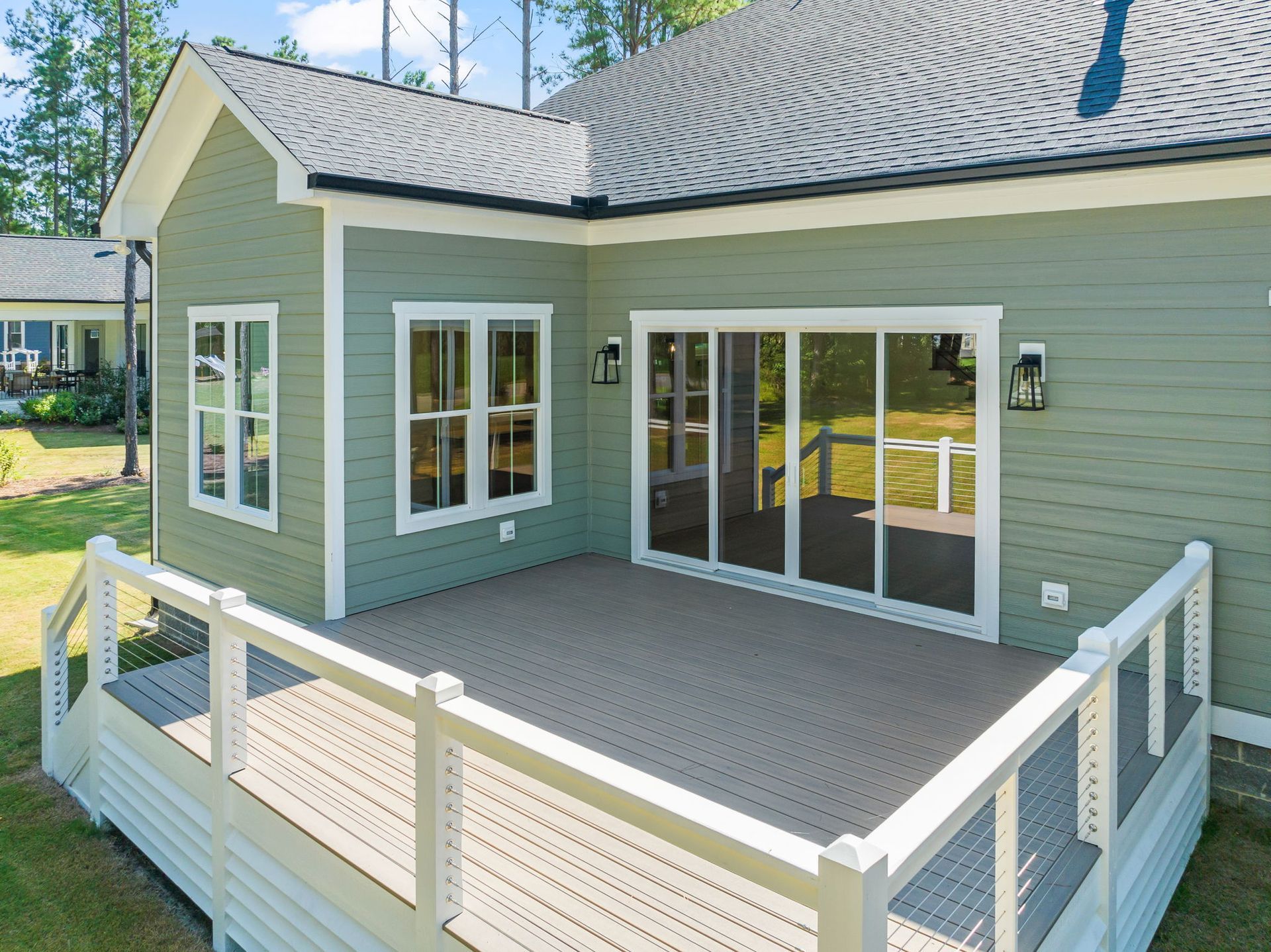 A deck and house exterior with sliding glass doors and white trim, surrounded by a white railing and green siding.