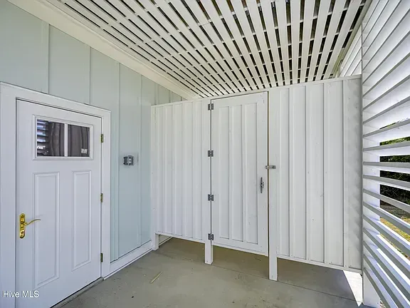 Outdoor shower with white walls, door, and slatted ceiling. Light blue wall and concrete floor.