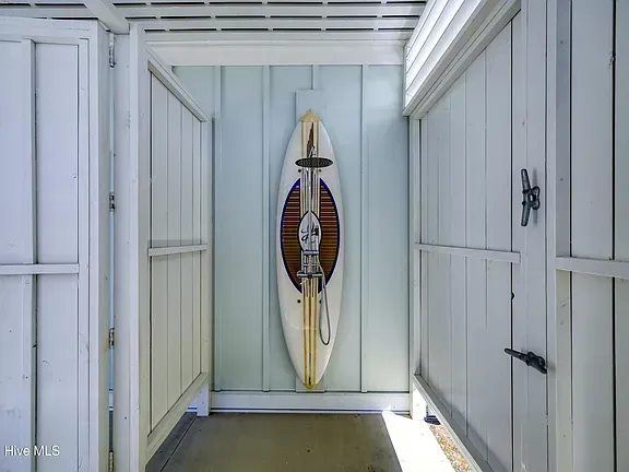 Outdoor shower with a surfboard mounted on the back wall. White walls and wooden doors.