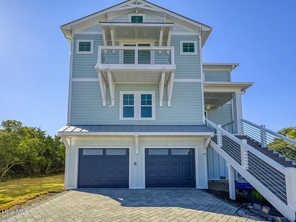 Light blue multi-story beach house with dark blue garage doors, and stairs.