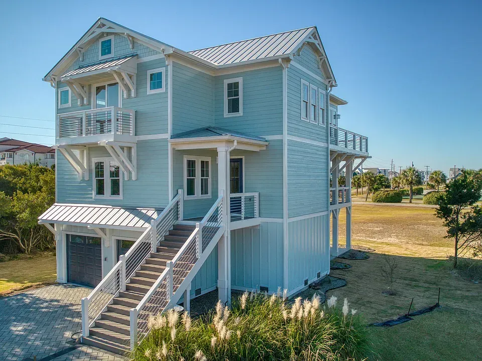 Light blue beach house with white trim, stairs, balconies, and a metal roof.