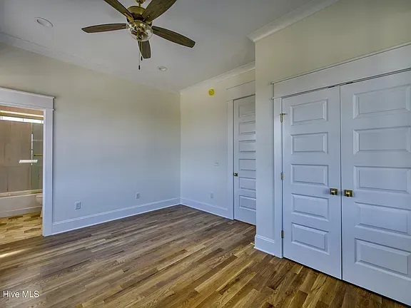 Bedroom with hardwood floor, white doors and trim, and a ceiling fan. A bathroom is visible in the corner.