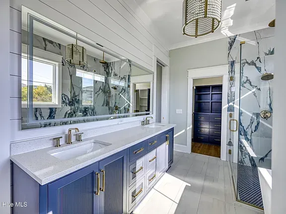 Bathroom with blue and white vanity, large mirror, marble shower, and chandelier.