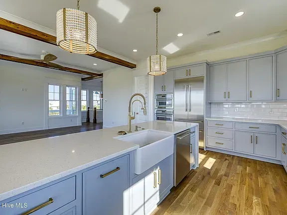 Spacious kitchen with blue cabinets, white countertops, and wood floors. Two crystal chandeliers hang above the island.