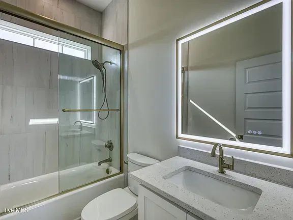 Modern bathroom with a bathtub, toilet, vanity, and large lighted mirror.