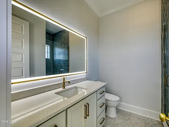 Bathroom with lit mirror over a white vanity, white toilet, gray walls, and marble floor.
