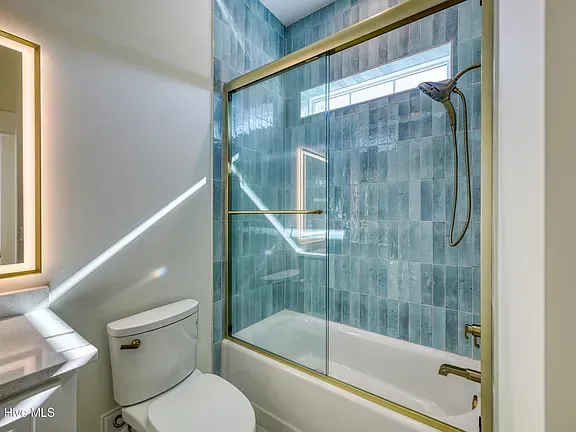 Bathroom with blue tiled shower, gold fixtures, and toilet.