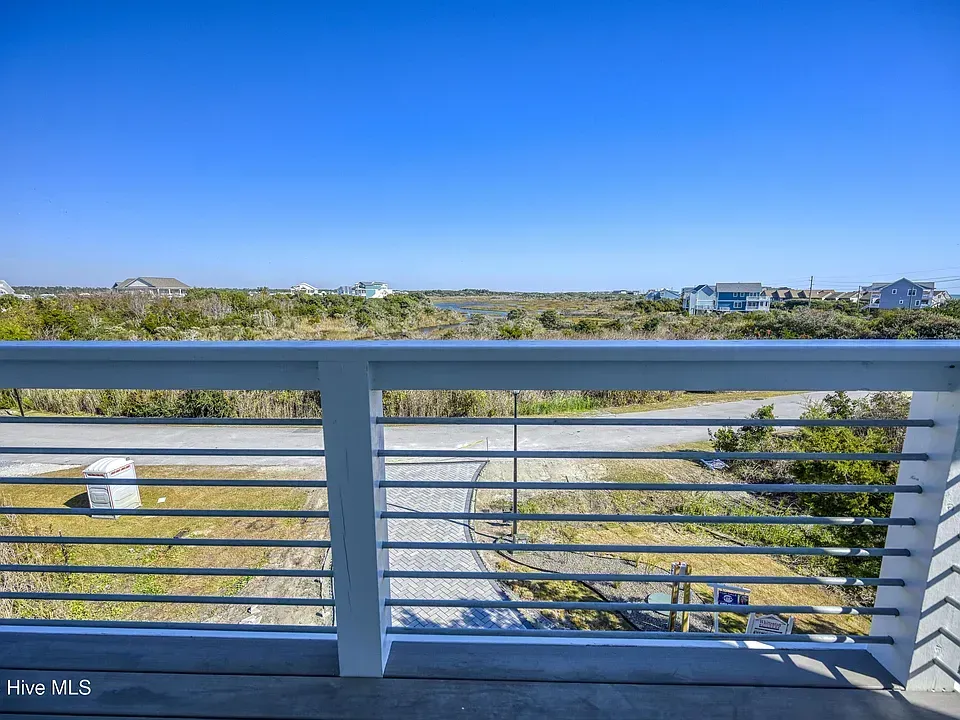 Balcony view of coastal landscape with blue sky. White railing frames the view of dunes, road, and houses.