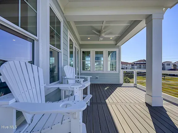 White Adirondack chairs on a covered porch with blue walls, windows, and a sunny view.