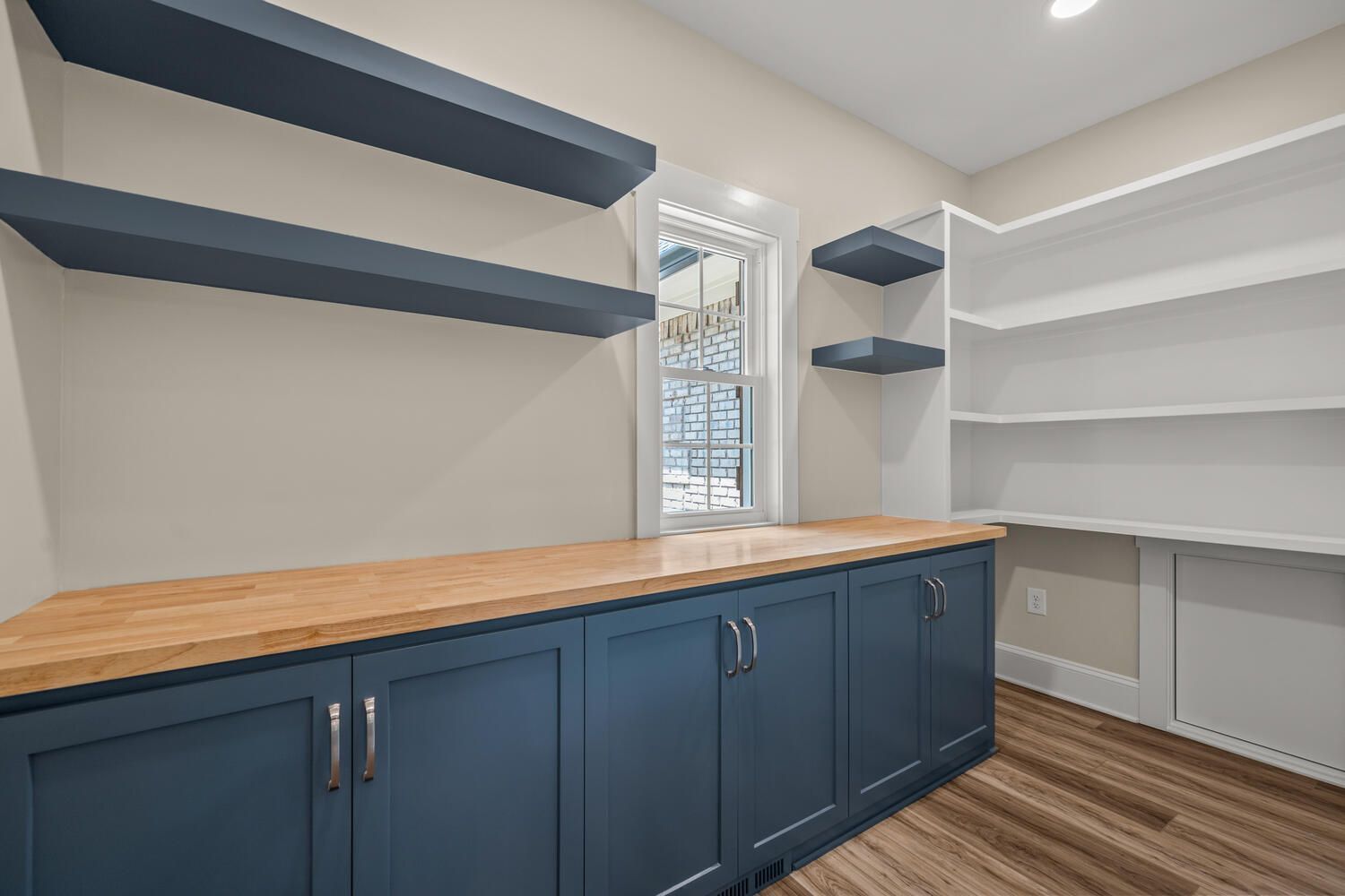 A room with blue cabinets and white shelves and a window.