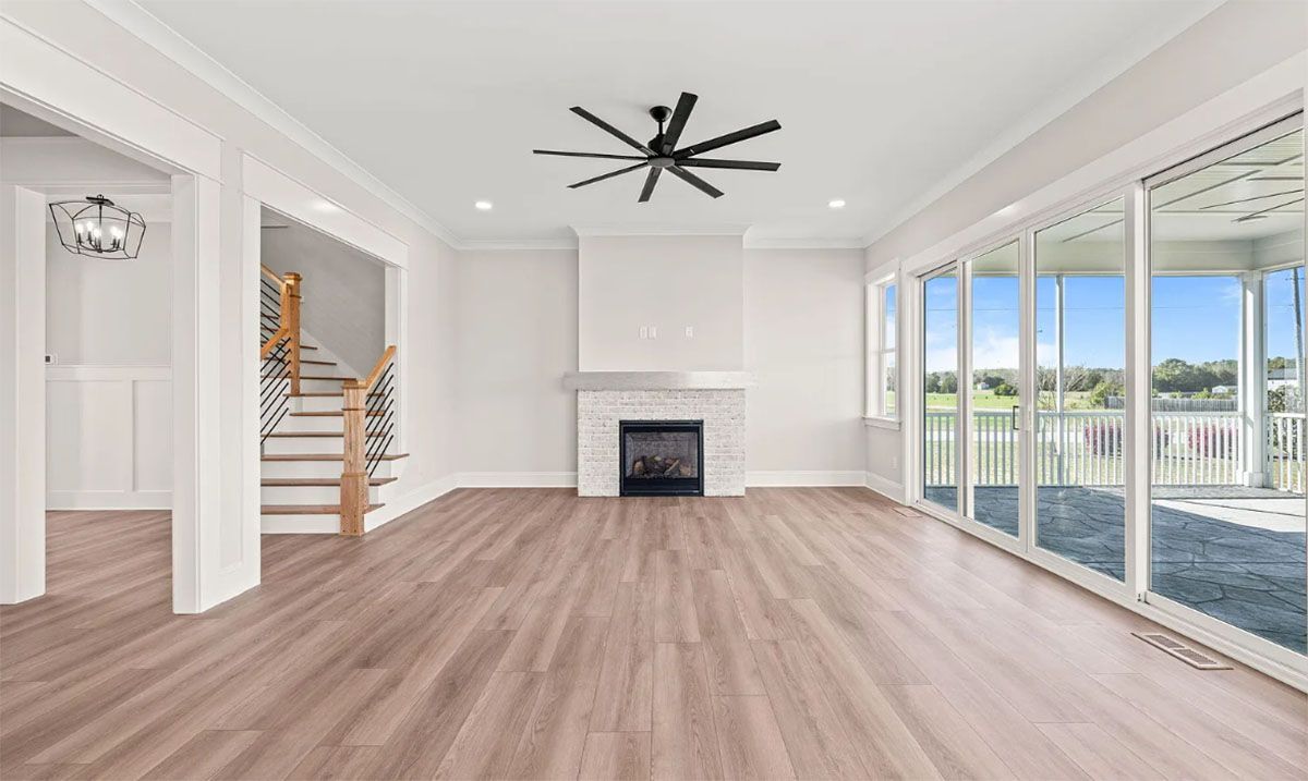 An empty living room with hardwood floors, a fireplace, and a ceiling fan