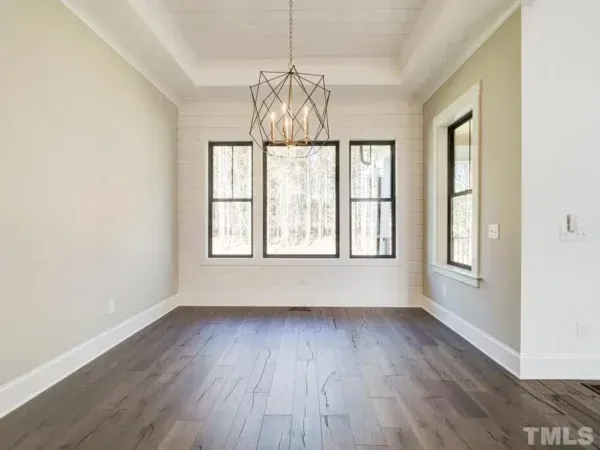 An empty dining room with hardwood floors and a chandelier hanging from the ceiling.
