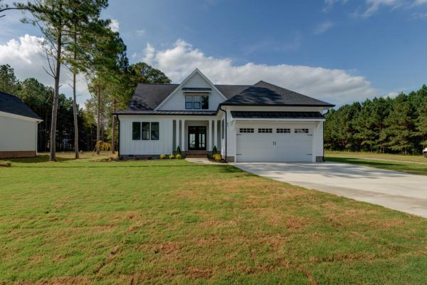 A white house with a black roof is sitting on top of a lush green field.