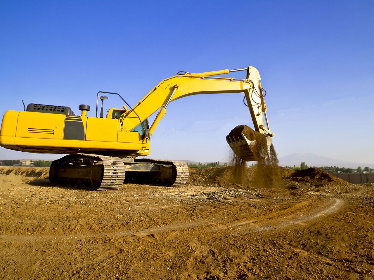 A yellow excavator is digging in a dirt field.