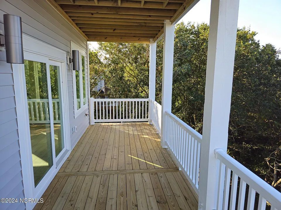 A large wooden deck with a white railing and trees in the background