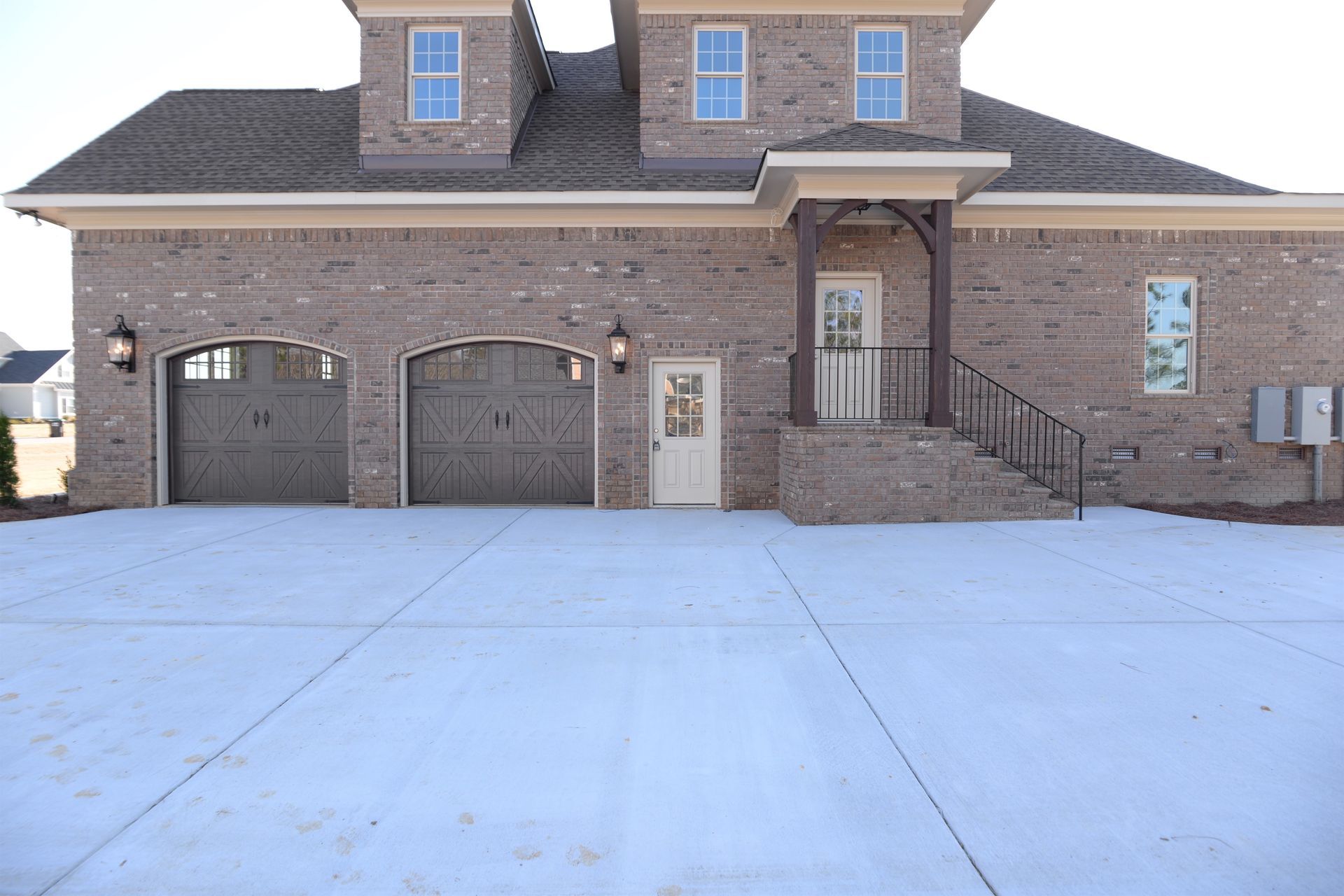 A large brick house with three garage doors and a concrete driveway.