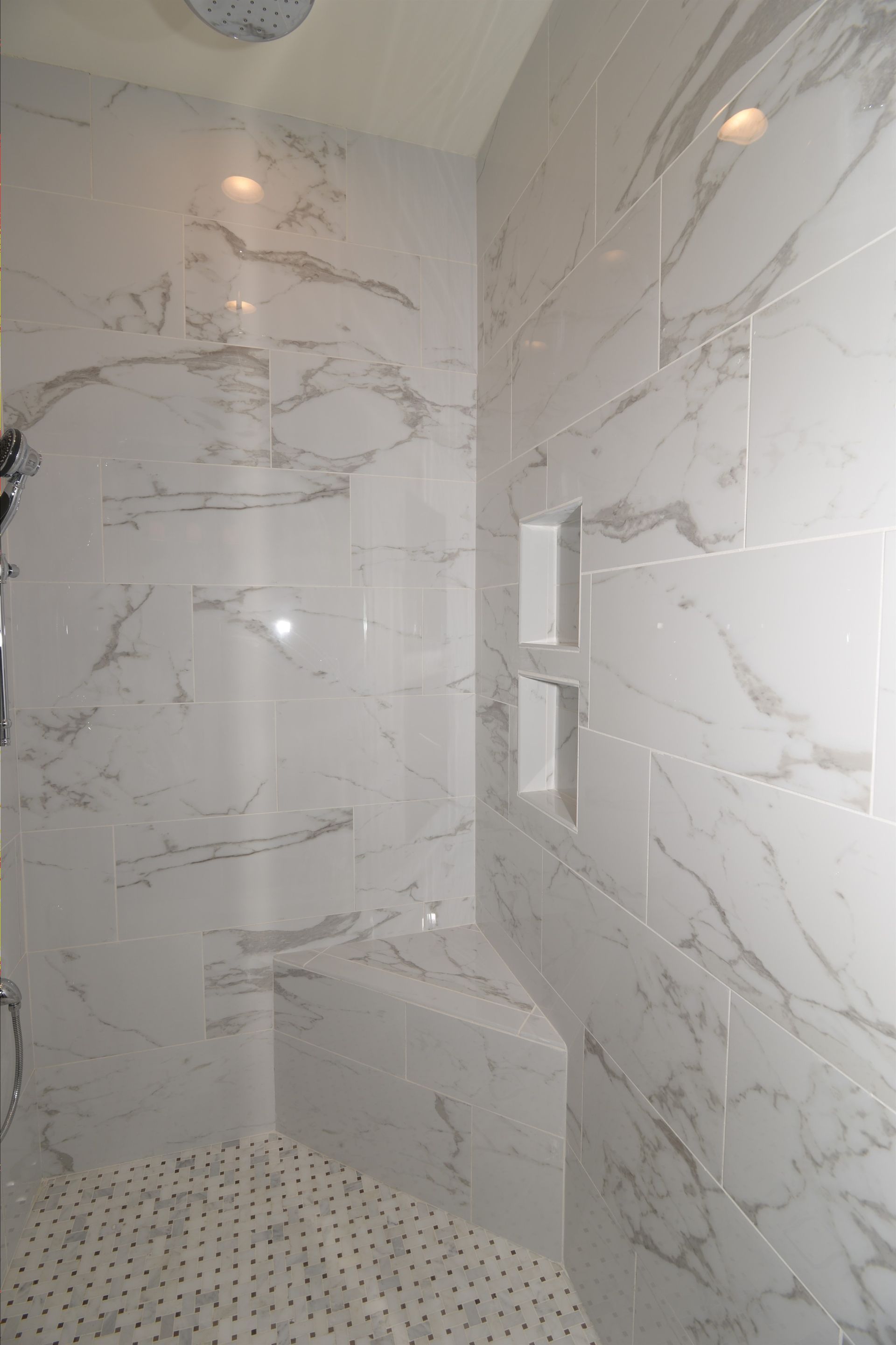 A bathroom with marble tiles and a walk in shower with a bench.