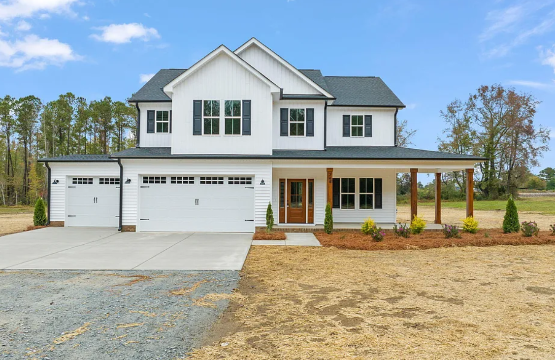 A large white house with a black roof is sitting on top of a dirt field.