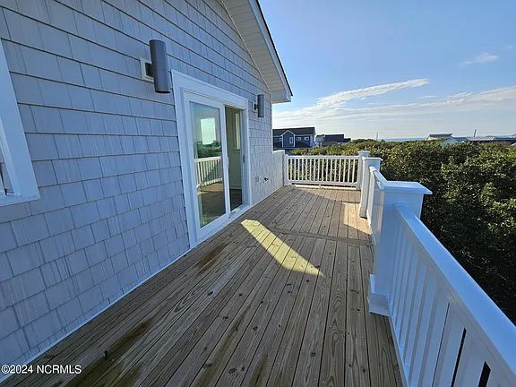 A large wooden deck with a white railing on the side of a house.