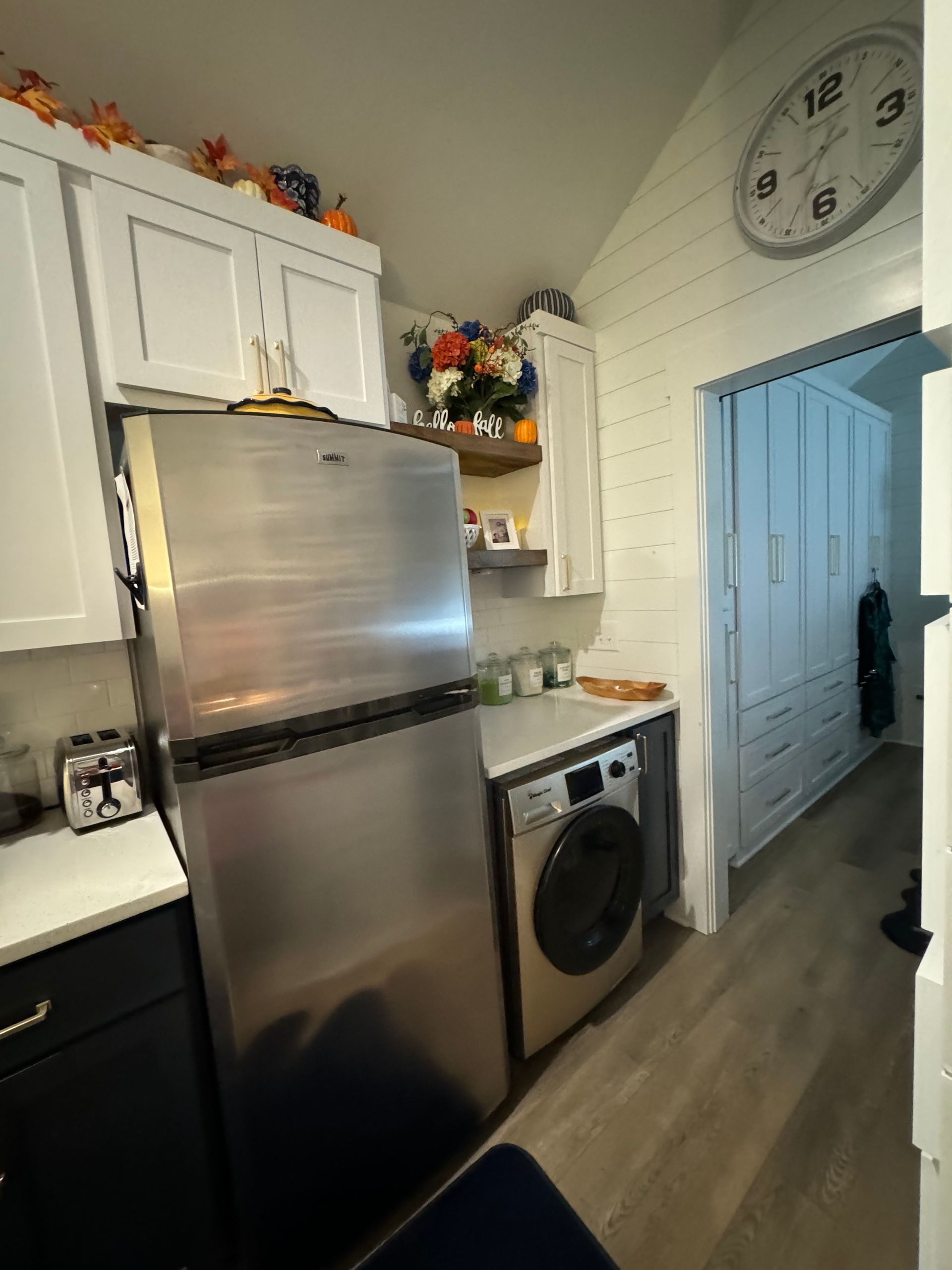 A kitchen with a refrigerator, washer and dryer, and a clock on the wall