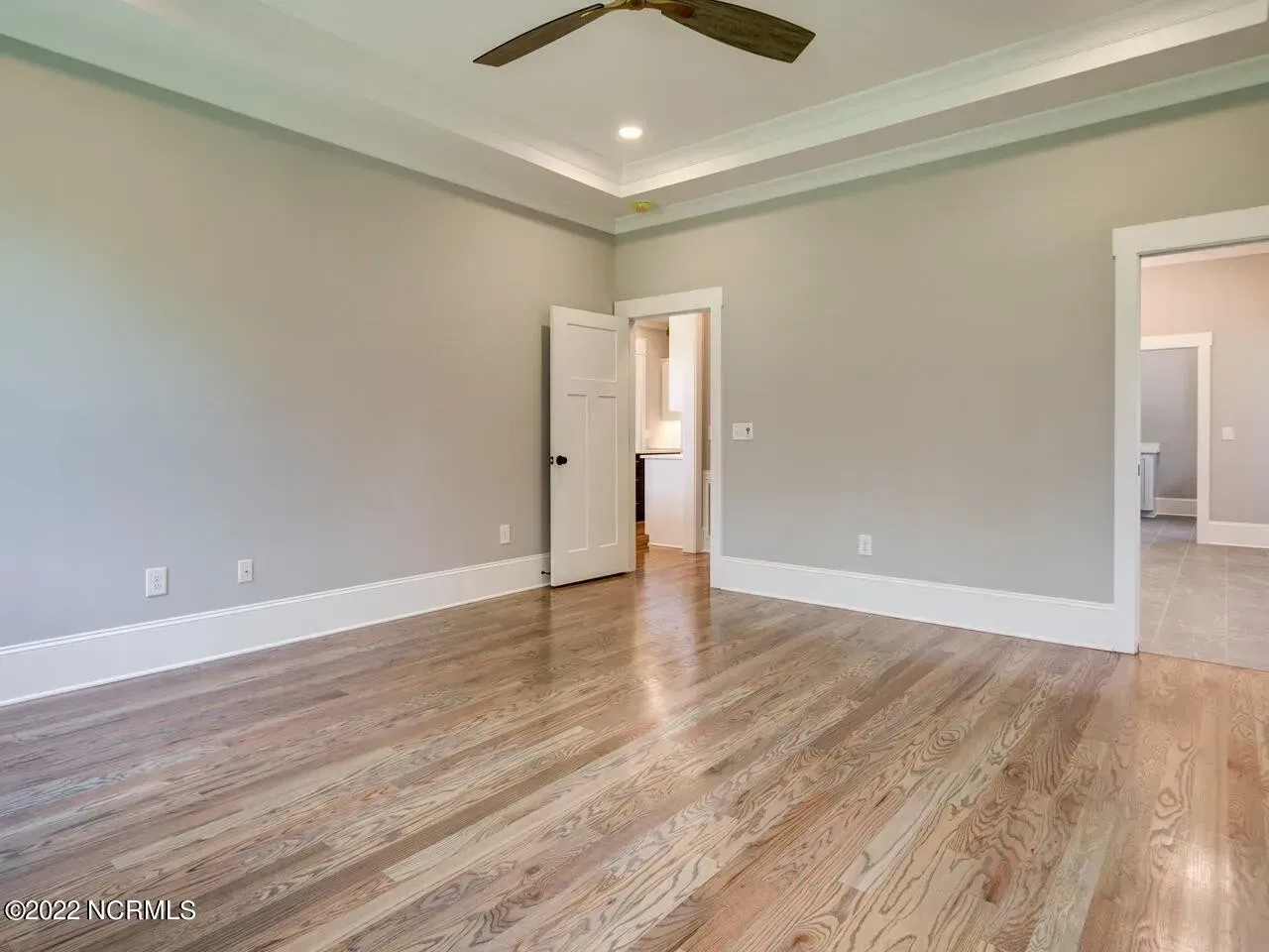 An empty bedroom with hardwood floors and a ceiling fan.