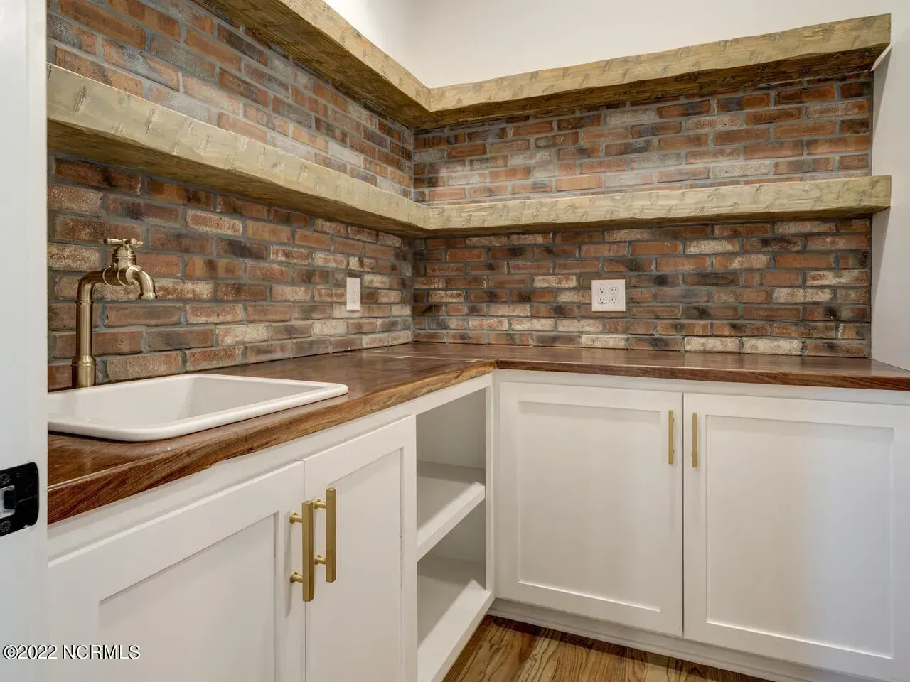 A laundry room with a sink and a brick wall.