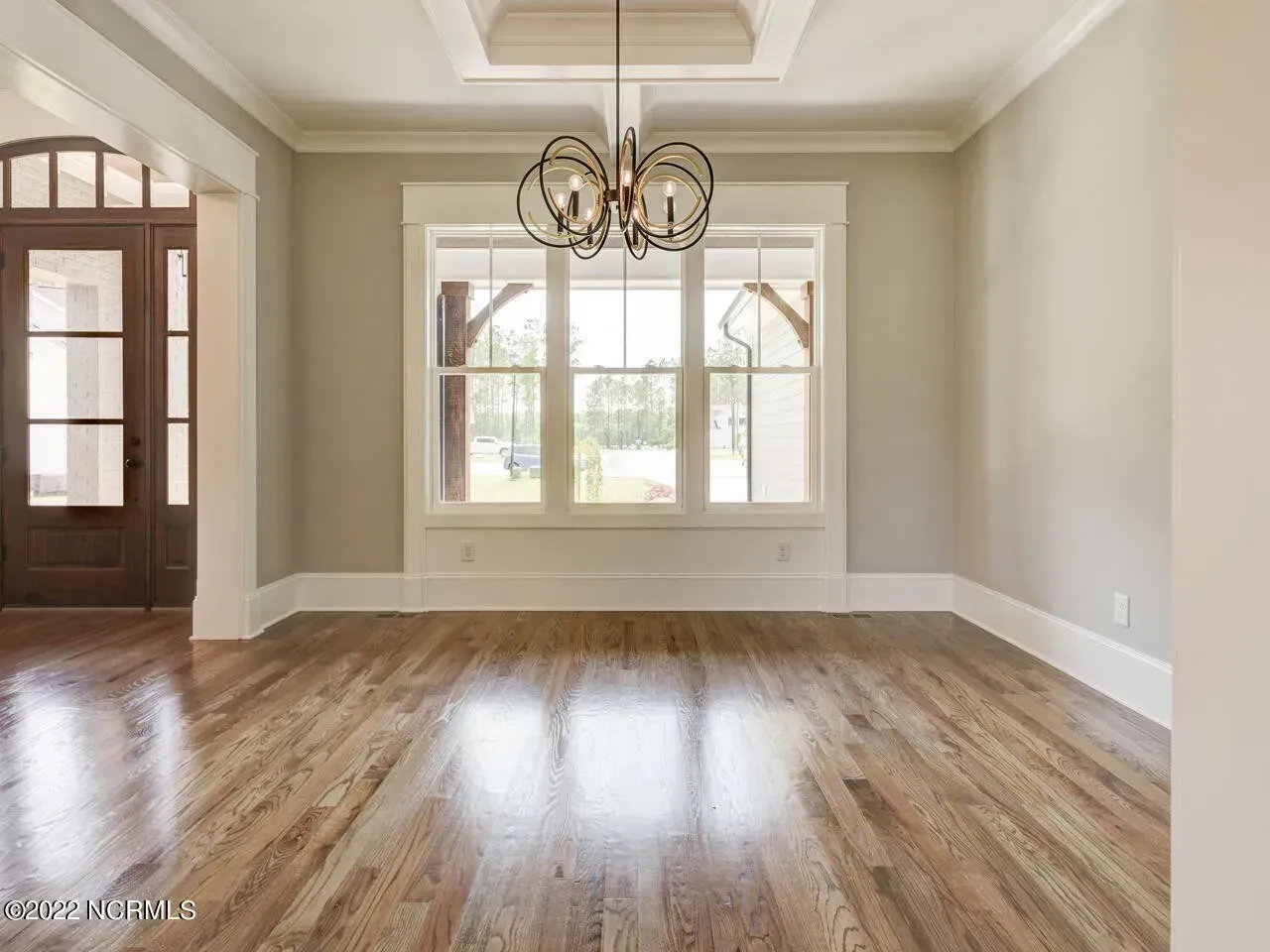 An empty room with hardwood floors and a chandelier