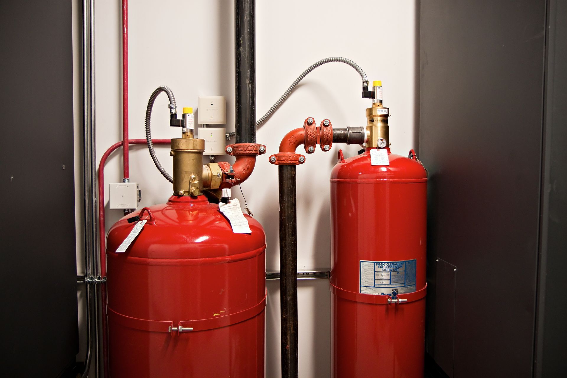 Two red fire suppression cylinders with brass valves and connected piping in an equipment room.