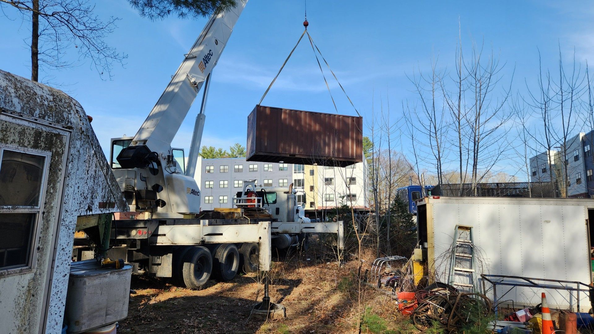 Crane lifting a large rusty shipping container in a yard on a clear day