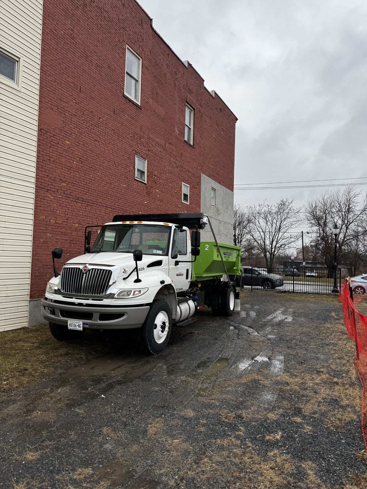 White dump truck beside a brick building on a gravel lot under a cloudy sky