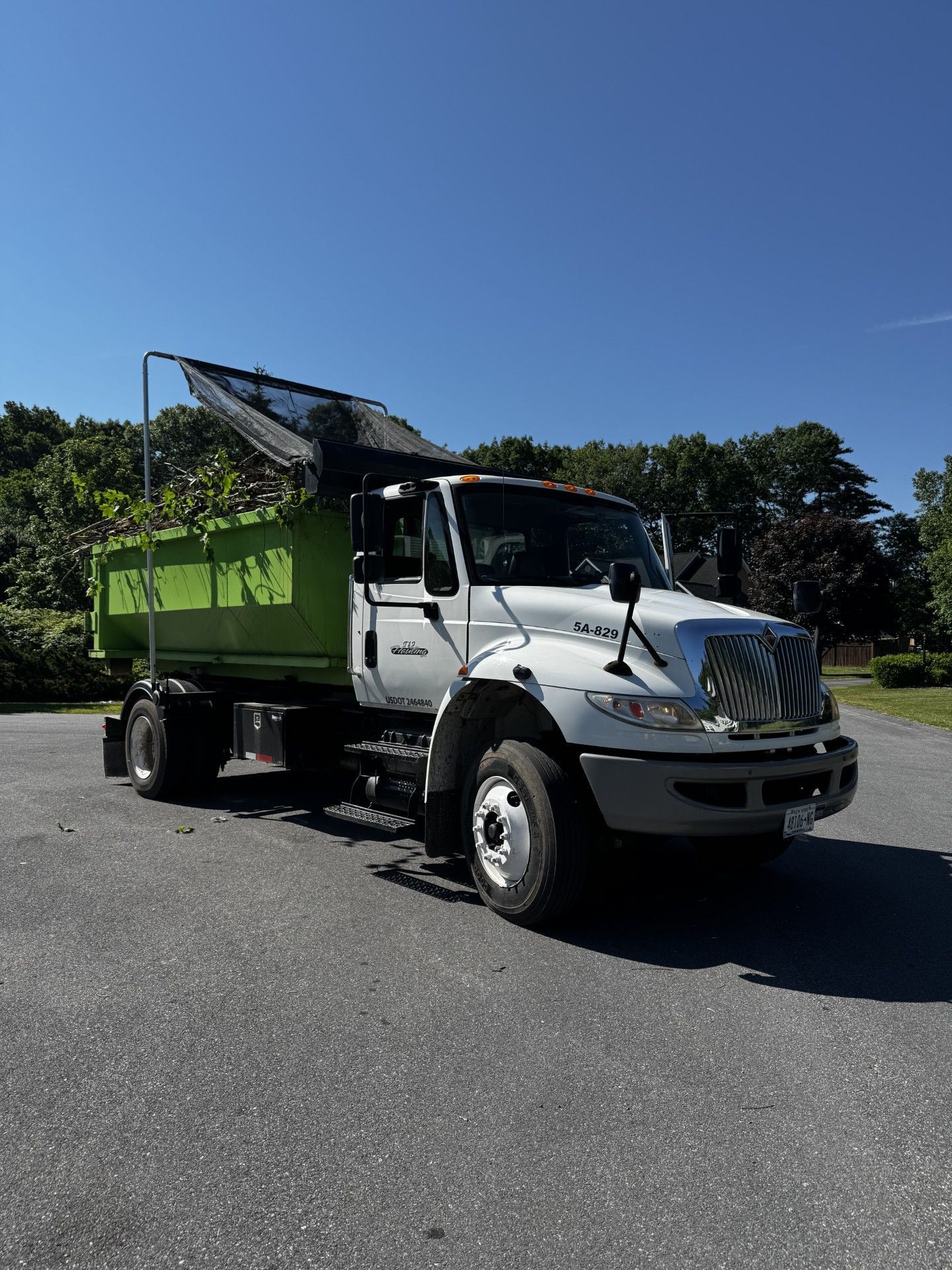 White dump truck with green trailer parked on a sunny lot under a clear blue sky