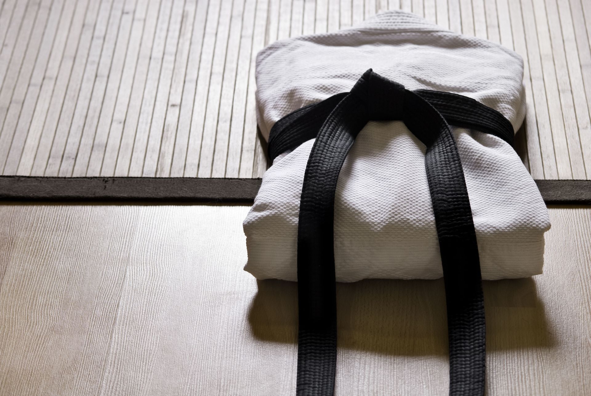 Folded white towel with a black ribbon on a tatami mat near a wooden floor separator