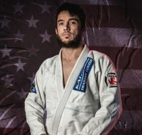 Man in a white martial arts gi posing in front of a faded American flag backdrop