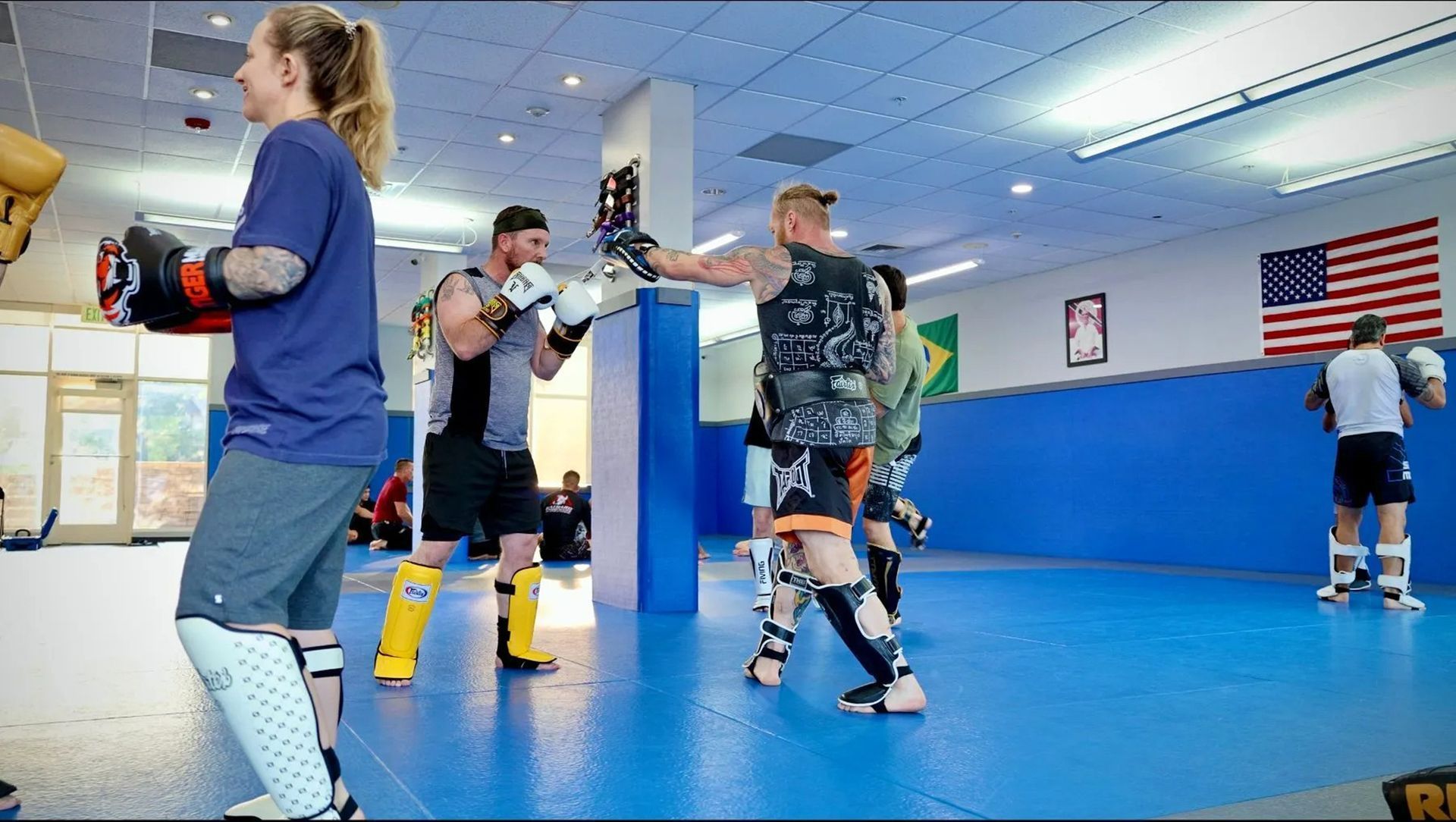 People practicing boxing drills in a blue gym with a U.S. flag on the wall
