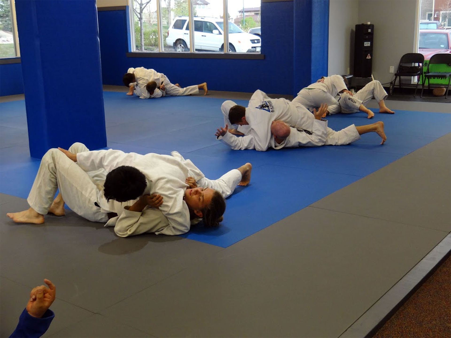 People practicing grappling drills on blue mats in a martial arts studio