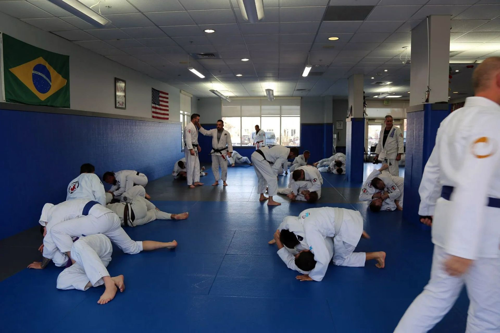 Martial arts class practicing grappling drills on blue mats in a gym with flags on the wall