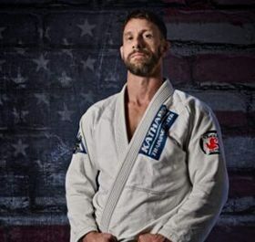 Man in a white martial arts gi posing before a faded American flag backdrop