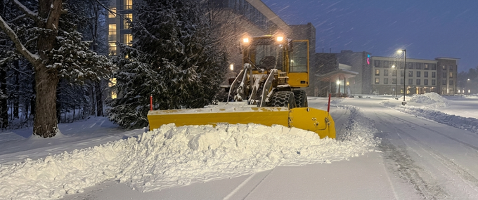 Black pickup truck plowing snow in a snowy parking lot under a cloudy sky