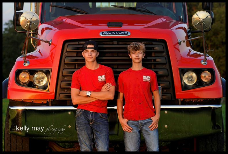Two men in red shirts standing in front of a large red truck.