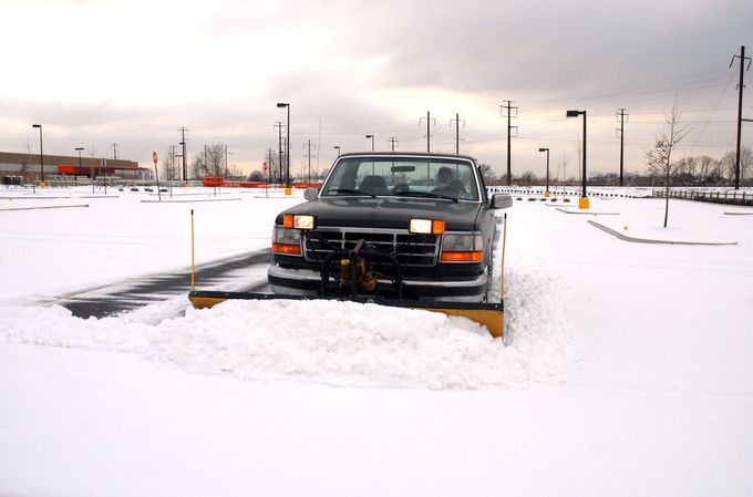 Black pickup truck plowing snow in a snowy parking lot under a cloudy sky