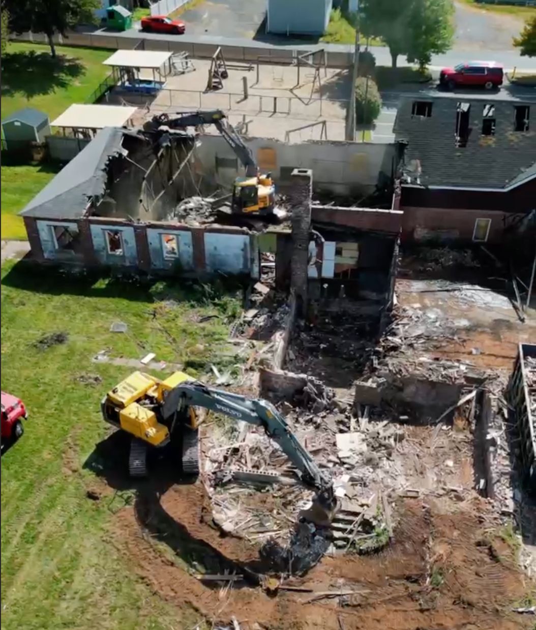 Aerial view of a demolition site with an excavator tearing down a burned brick building.