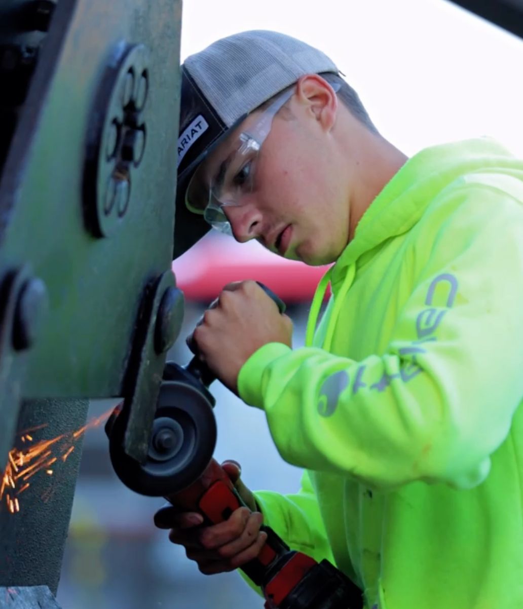 Worker in neon green hoodie using an angle grinder on metal, with sparks flying indoors.